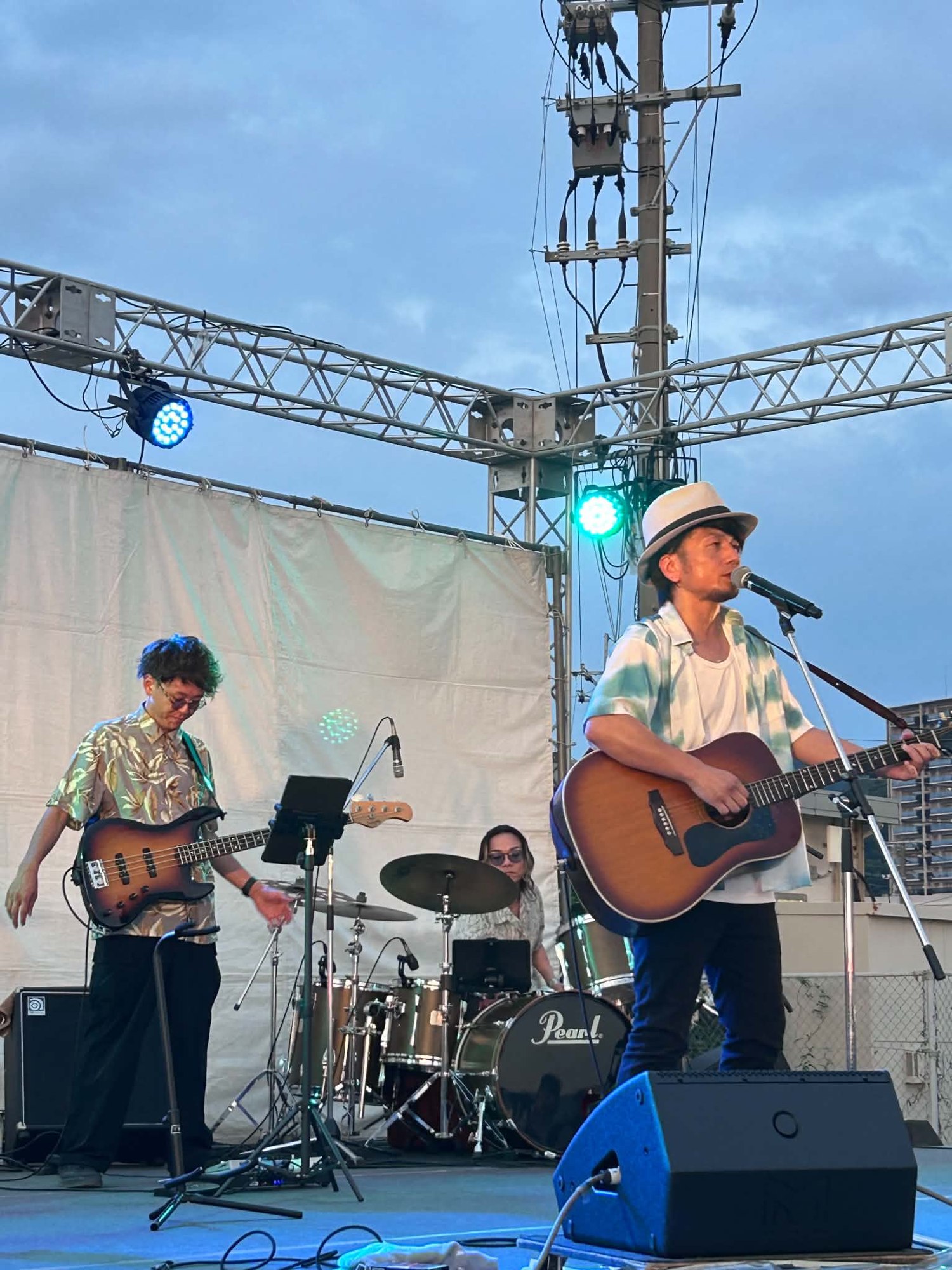 夕暮れの野外ステージでギターを弾きながら歌う池端克章とバンドメンバー